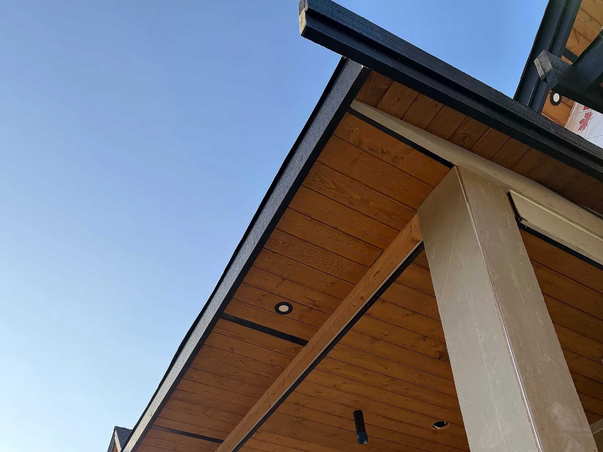 Clear cedar tongue-and-groove porch eave meeting a square column under black fascia, Langley BC