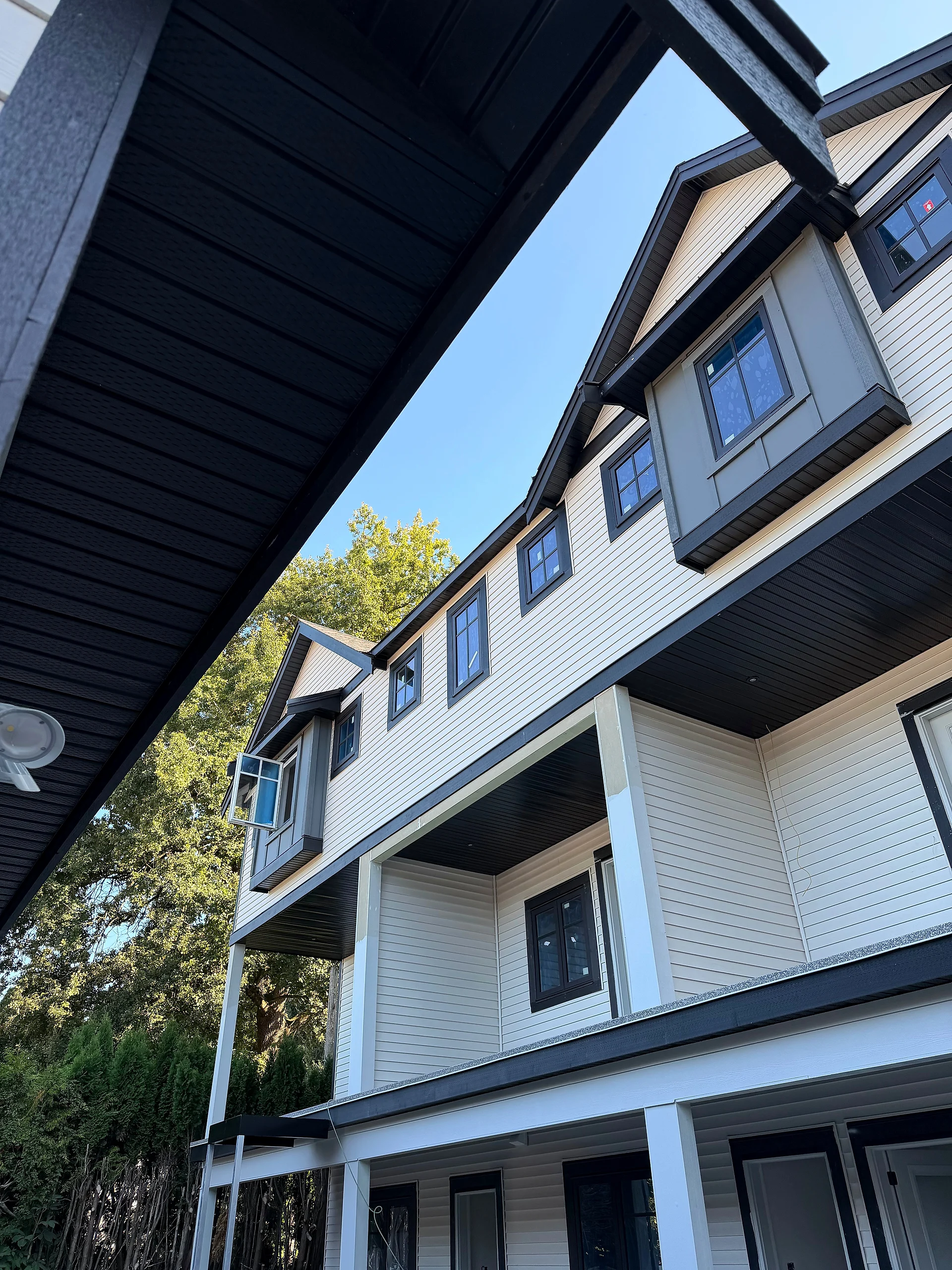 Rear townhouse block in cream lap siding with grey panel dormers and black soffits, looking up from the porch, Abbotsford BC
