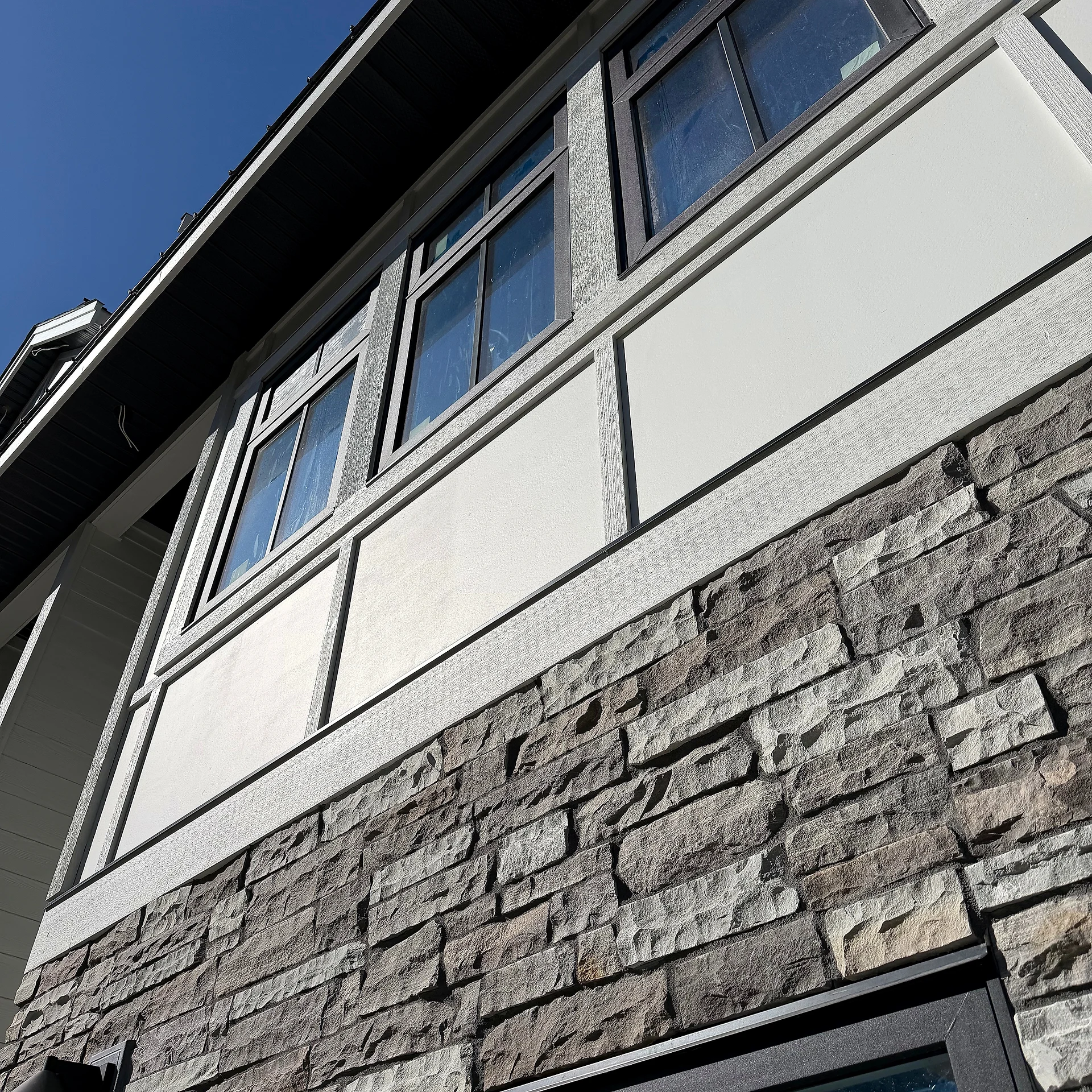 White panel and batten finishing above a stone base at the corner of a townhouse block, Abbotsford BC