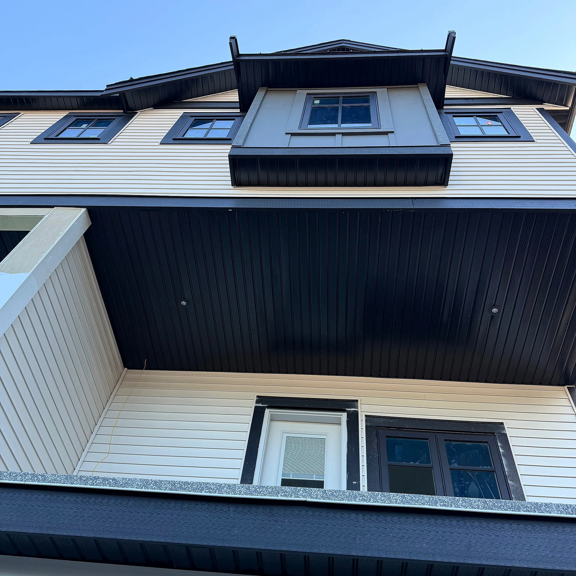 Grey panel dormer and black soffit above cream lap siding, looking straight up, Abbotsford BC