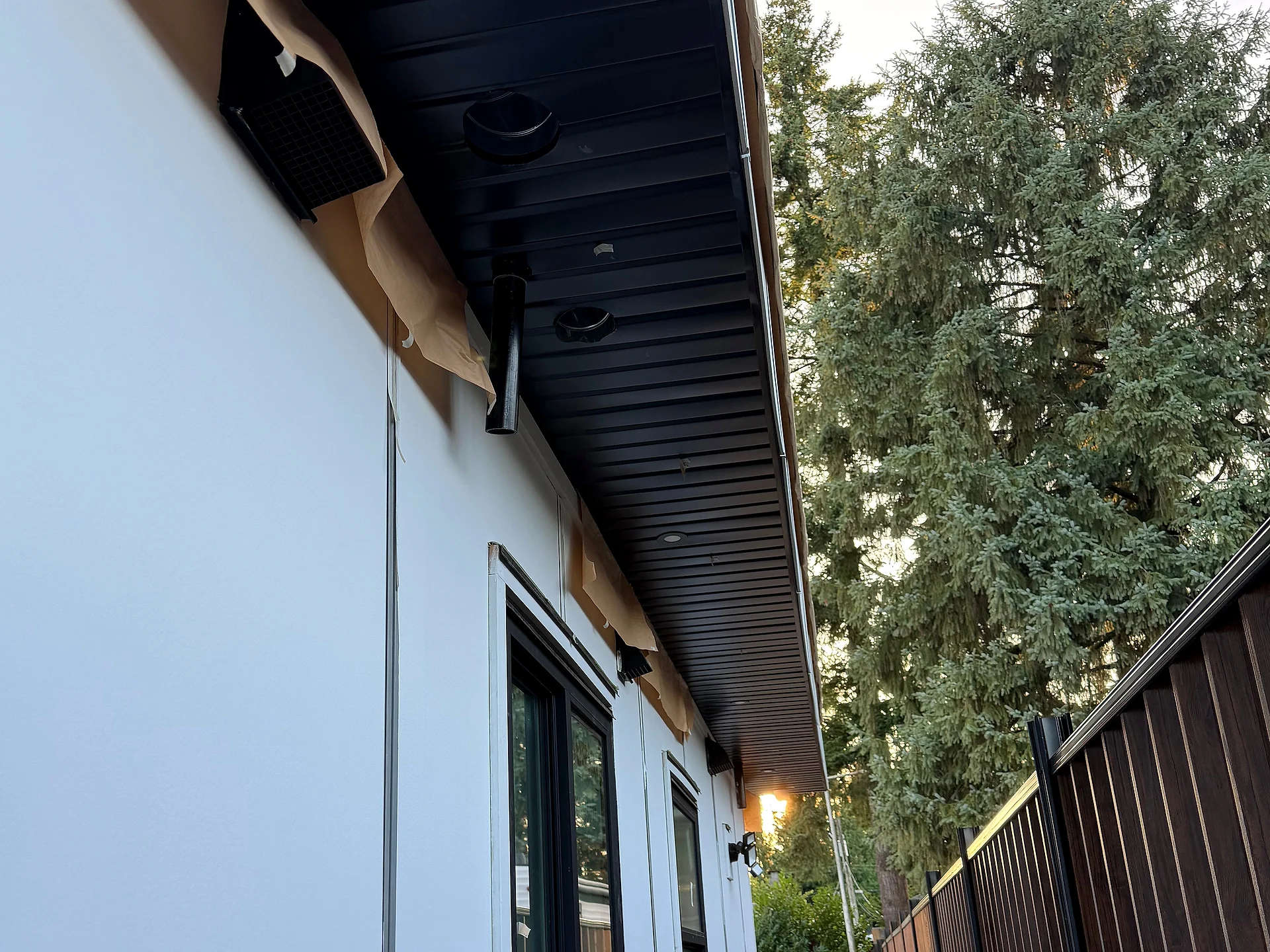 Side passage with white panel reveals running true from eave to ground, black soffit above, Coquitlam BC