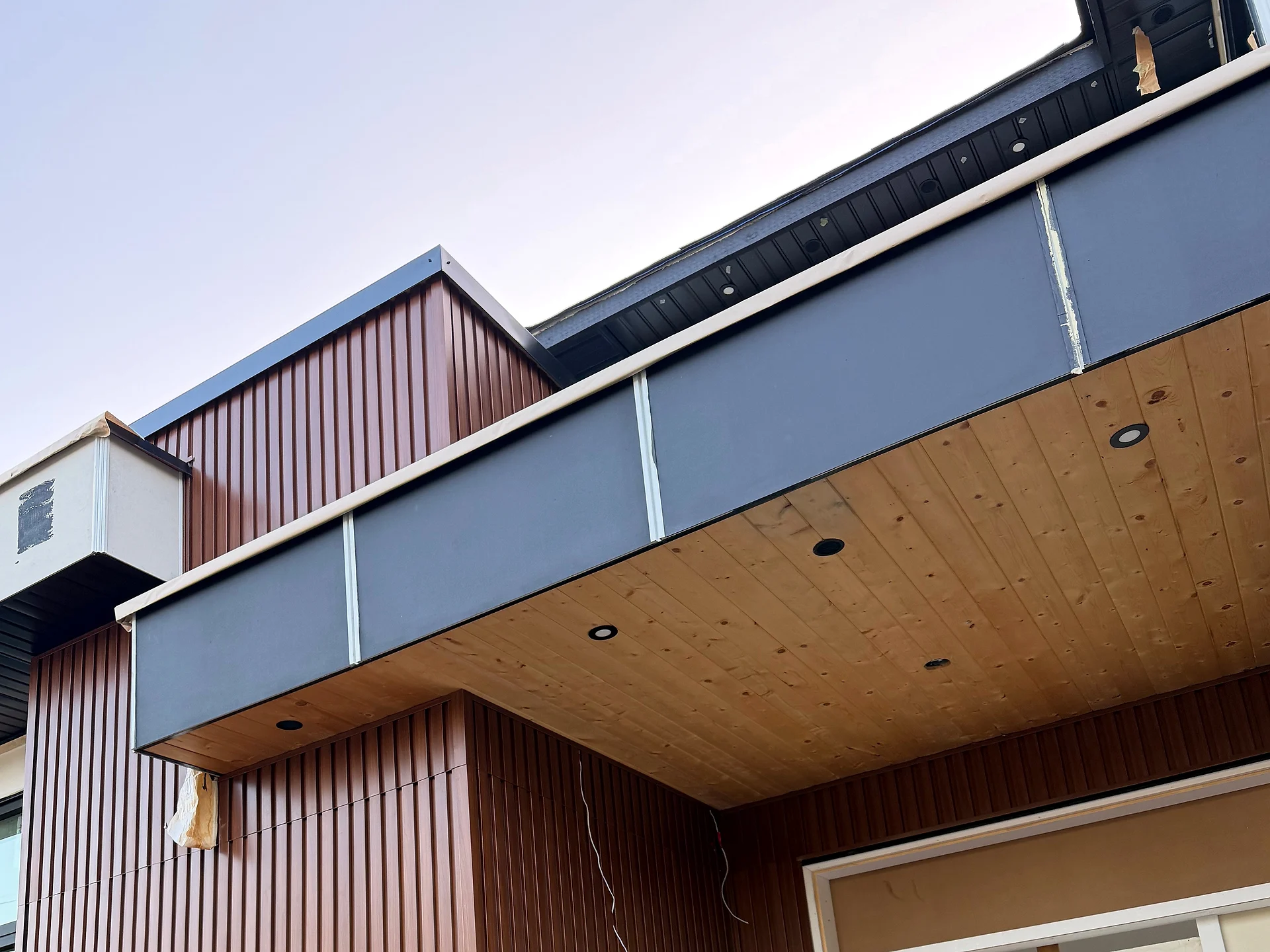 Wood tongue-and-groove entry ceiling with recessed lights under black fascia, fluted cladding either side, Coquitlam BC