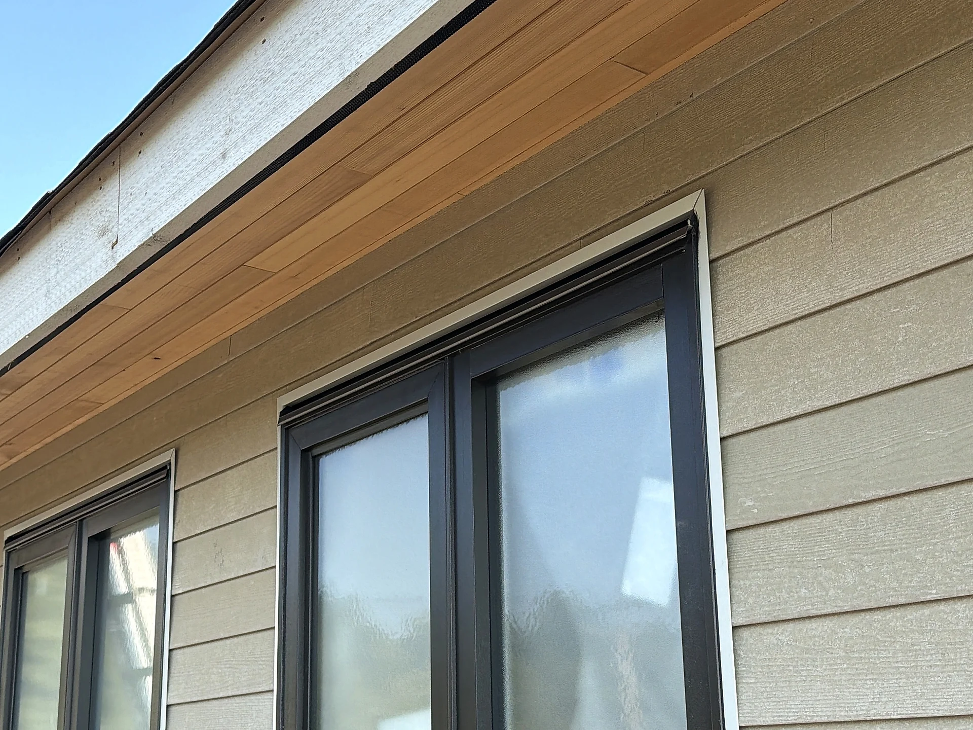 Cedar soffit and fascia over a black-framed window in tan lap siding, North Vancouver BC