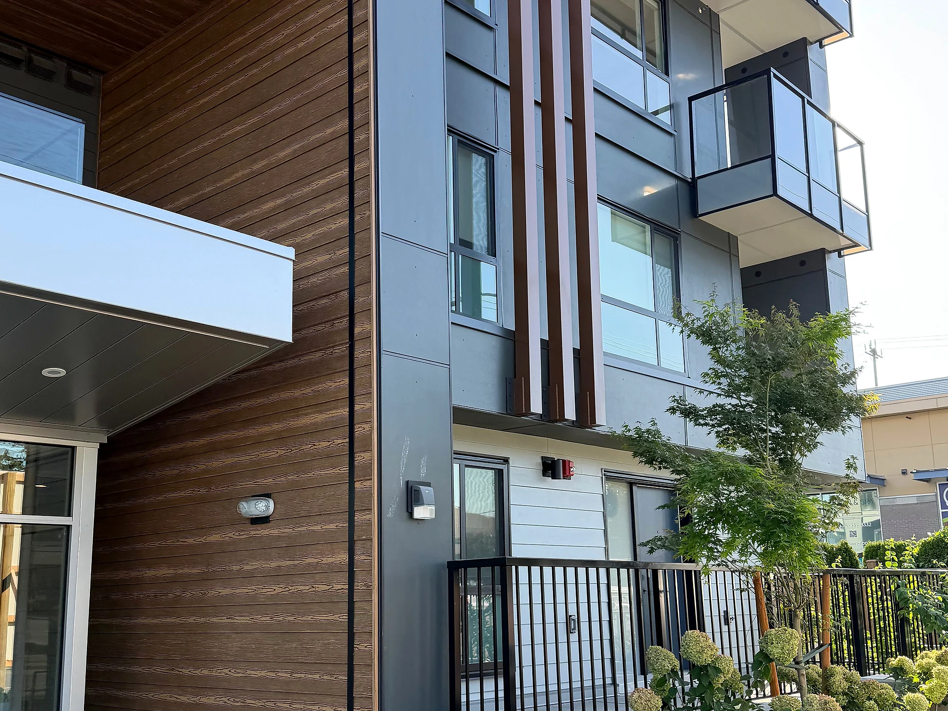 Mid-rise lobby entry with a wood-clad canopy, bench and hydrangeas, South Surrey BC