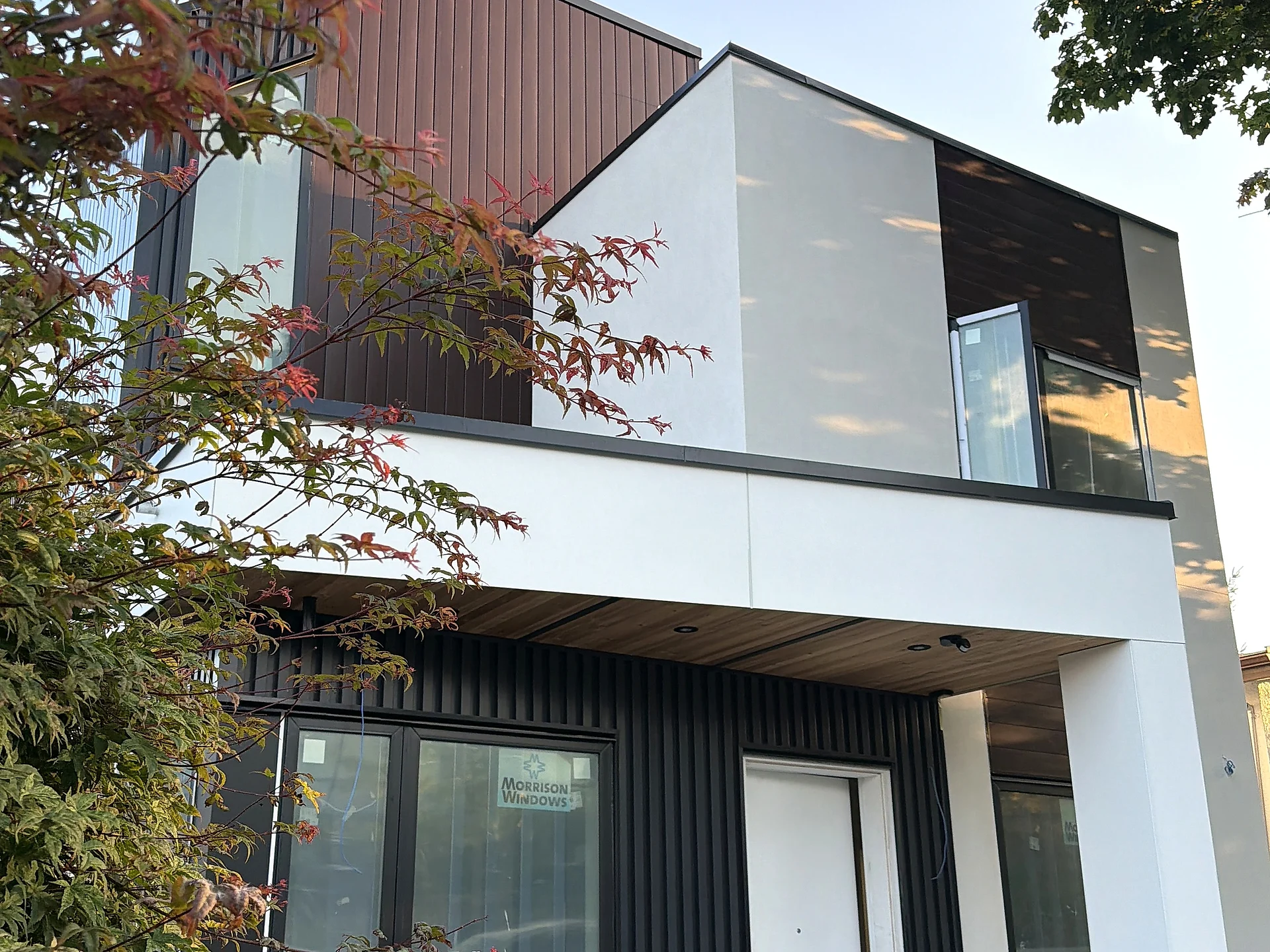 Modern infill home with a cedar entry soffit and black vertical cladding, seen past a Japanese maple, Vancouver BC