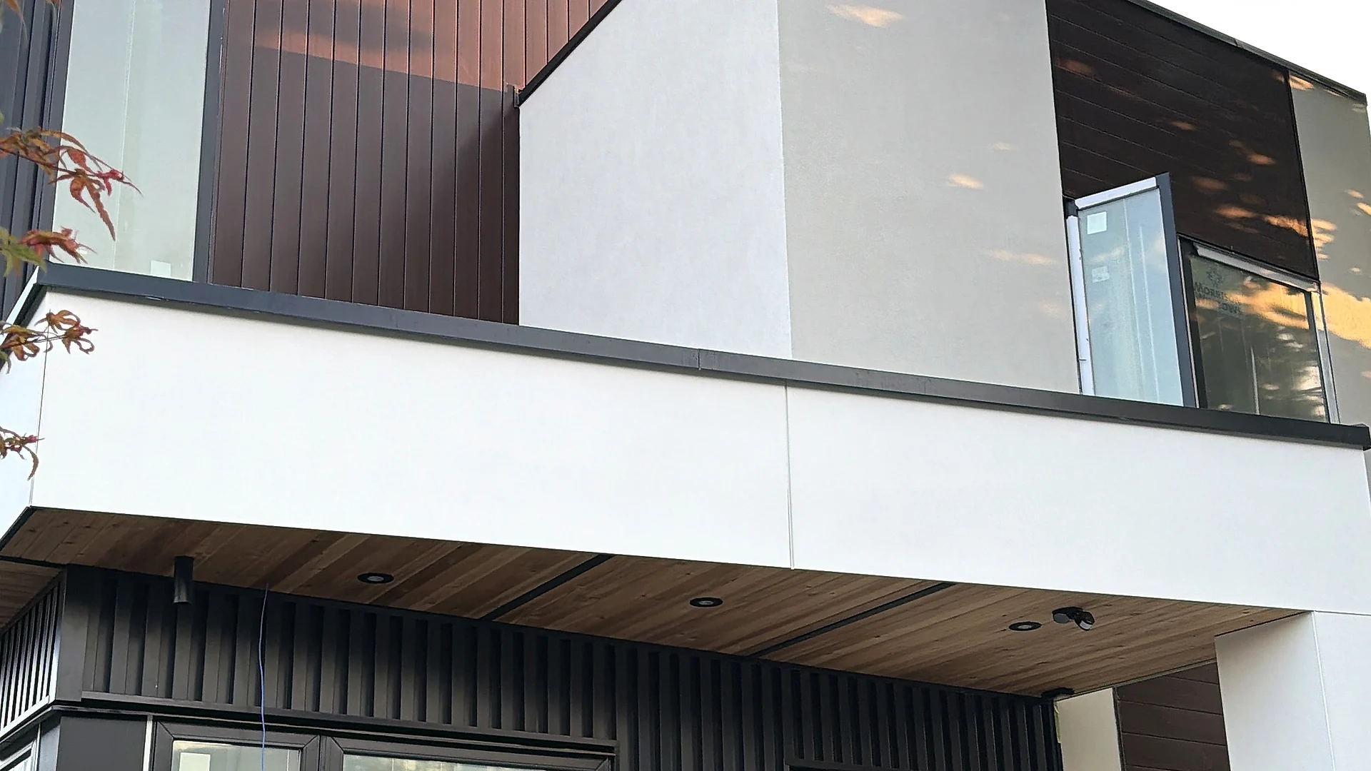 Modern infill home: white panel volume, dark vertical cladding above, black vertical cladding and a cedar soffit below, Vancouver BC — exterior finishing by Moonrise Construction