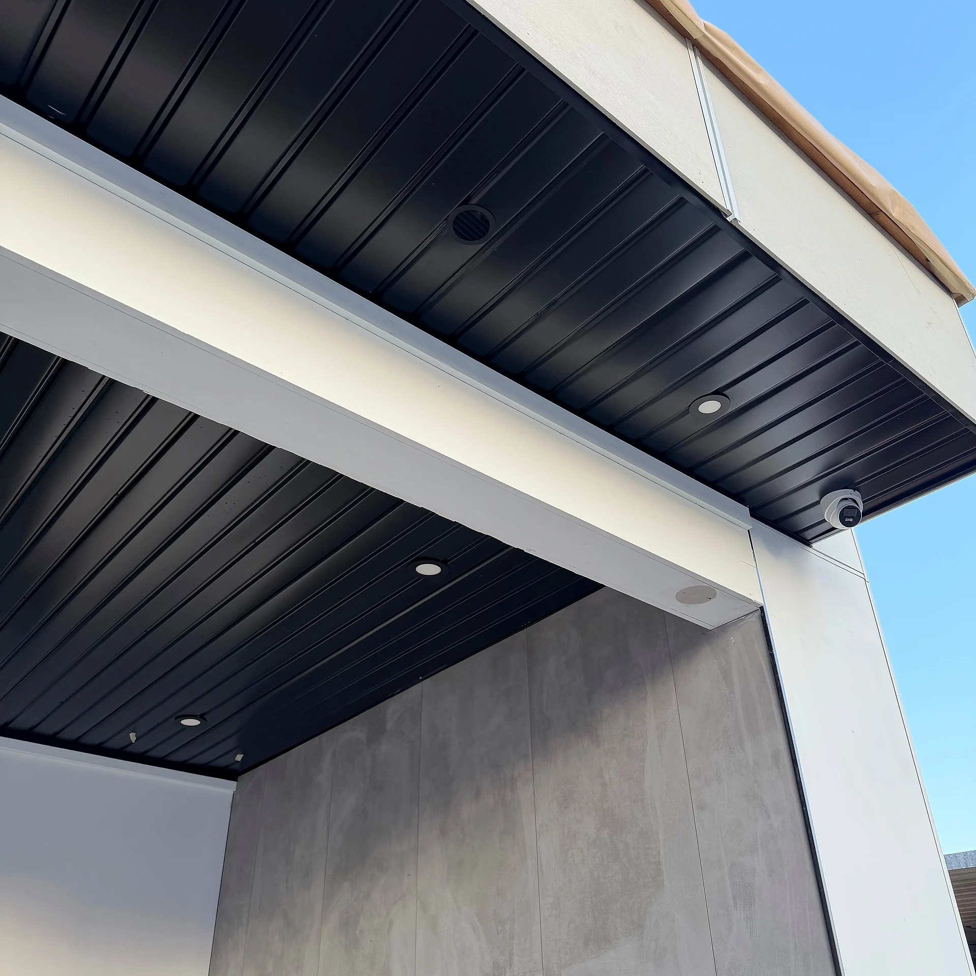Black ribbed metal soffit over a white column and grey panel wall at a covered patio corner, Coquitlam BC
