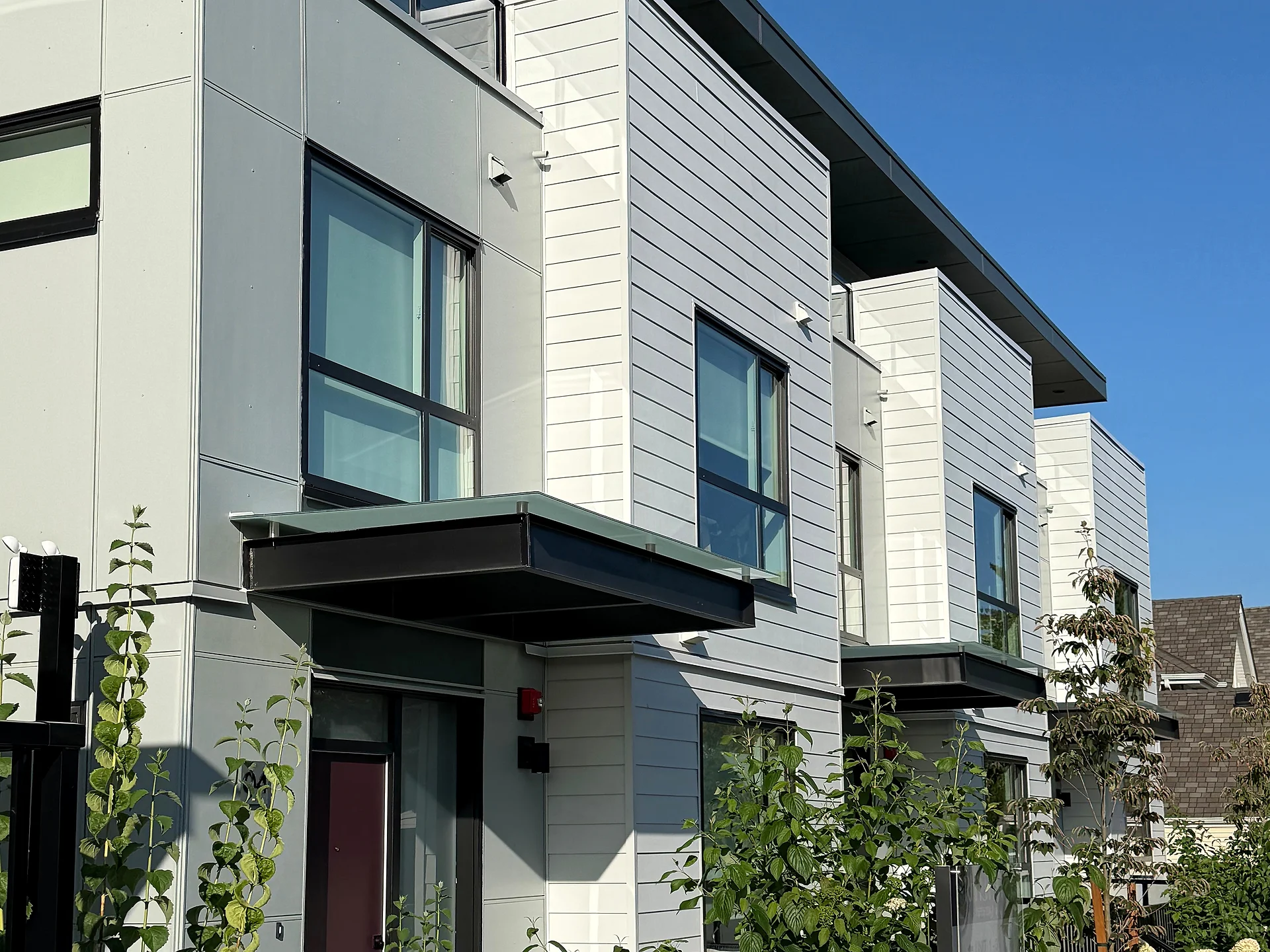 Townhouse row with grey lap siding, white panel and cantilevered entry canopies, South Surrey BC